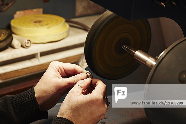 A person holding a small ring and using a grinding machine to shape and polish it. Workbench in a jewellers.