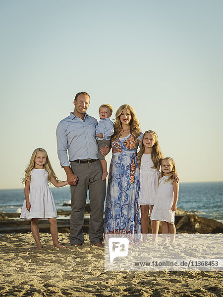 Familie mit Kindern (12-17 Monate  4-5  6-7  8-9) am Strand stehend mit Meer im Hintergrund