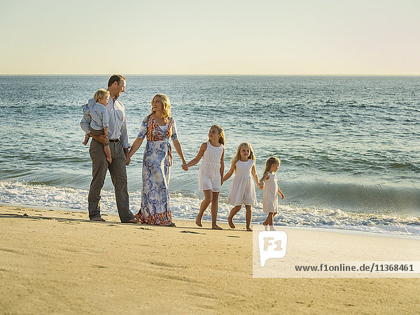 Familie mit Kindern (12-17 Monate  4-5  6-7  8-9) beim Spaziergang am Strand mit Meer im Hintergrund