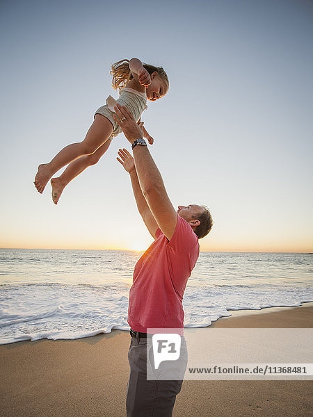 Vater wirft Tochter (4-5) am Strand in die Luft