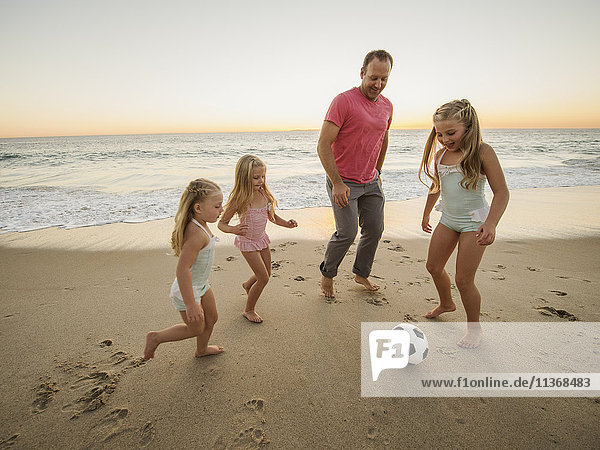 Vater mit Kindern (4-5  6-7  8-9) beim Fußballspielen am Strand