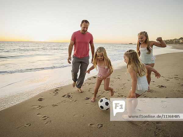 Vater mit Kindern (4-5  6-7  8-9) beim Fußballspielen am Strand