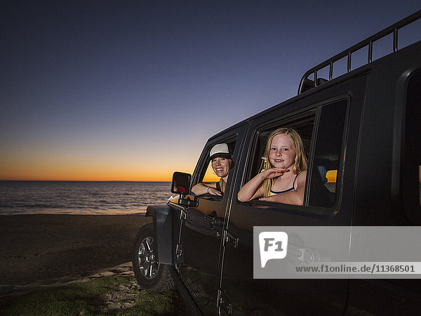 Mother and daughter (4-5) sitting in car on beach