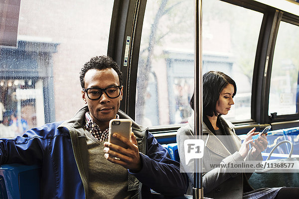 A young man and a young woman sitting on public transport looking at their cellphones.
