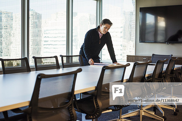 A man standing at a table in a meeting room looking down at an open book.