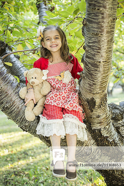 Girl with teddy bear sitting on tree