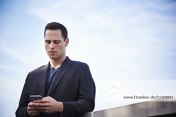 Ein junger Mann steht auf einem Dach und schaut auf ein Mobiltelefon.