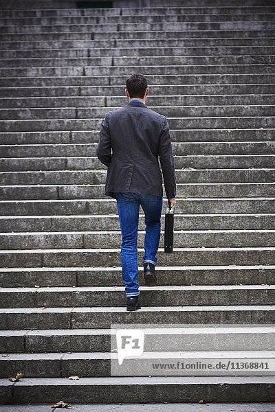 A young man walking up on a flight of steps holding a briefcase  seen from behind.