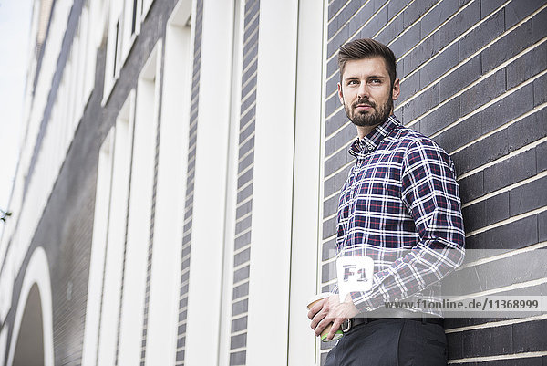Young man leaning against wall and drinking coffee