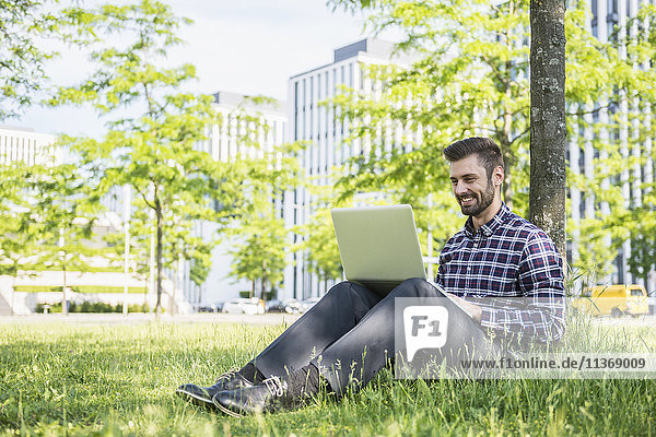 Junger Mann arbeitet am Laptop und sitzt im Park