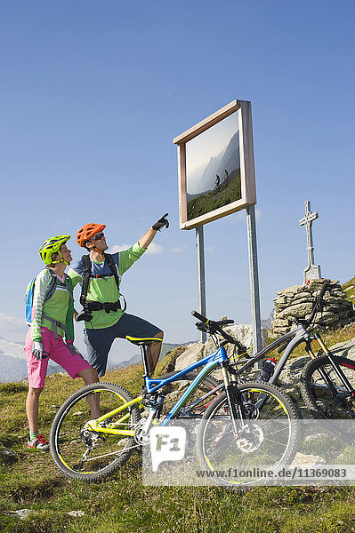Young couple of mountain bikers watching information board on uphill  Zillertal  Tyrol  Austria