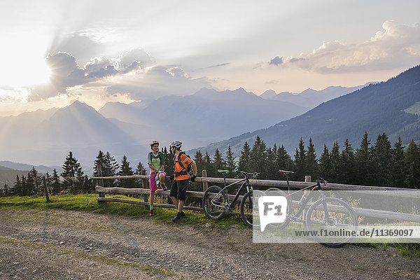 Young couple of mountain bikers standing by wooden fence during sunset  Zillertal  Tyrol  Austria