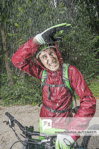 Mountainbiker im Regen stehend mit Hand über Kopf  Kampenwand