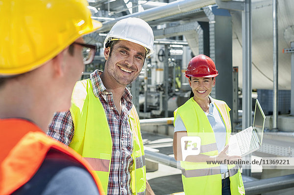 Zufriedener Ingenieur mit seinen Kollegen bei einer Besprechung mit Laptop im geothermischen Kraftwerk
