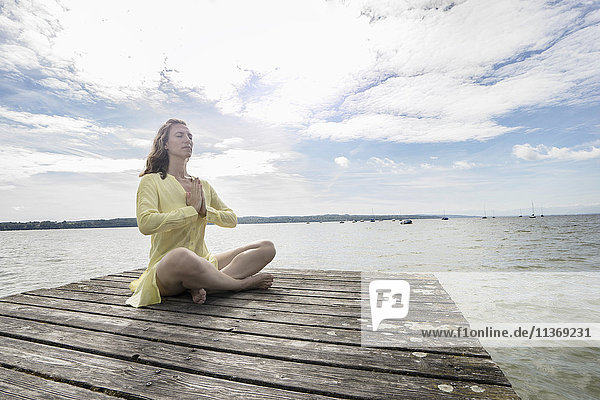 Frau beim Yoga im Lotussitz auf dem Steg am See  Ammersee  Oberbayern  Deutschland