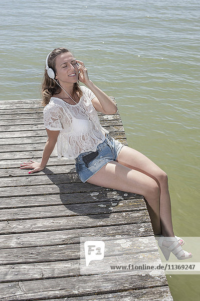 Woman listening to music and sitting on boardwalk at the lake  Ammersee  Upper Bavaria  Germany