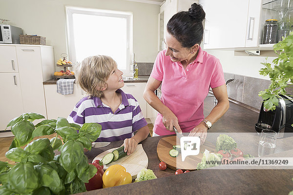 Woman with her son chopping vegetables in kitchen