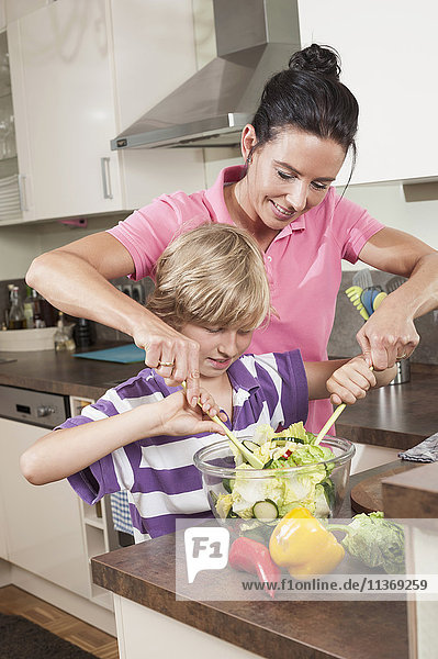 Frau mit ihrem Sohn bei der Zubereitung von Salat in der Küche