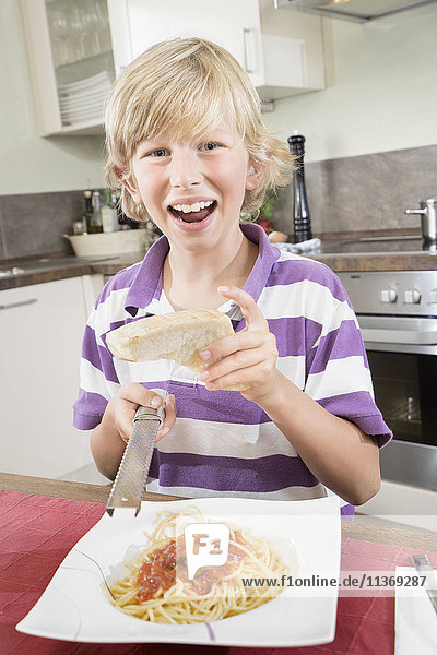 Porträt eines glücklichen Jungen  der Käse über Spaghetti reibt