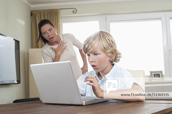 Shocked woman watching her son using laptop in living room