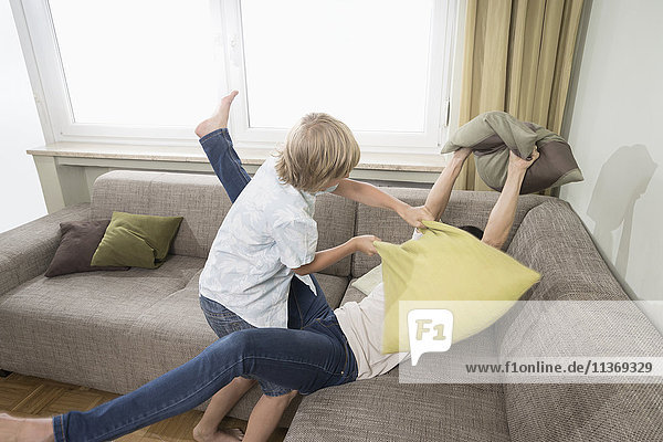 Frau kämpft mit ihrem Sohn im Wohnzimmer mit Kissen