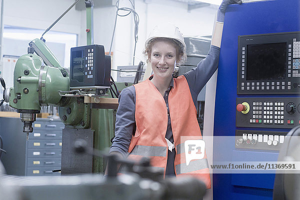 Young female engineer standing at CNC machine in an industrial plant