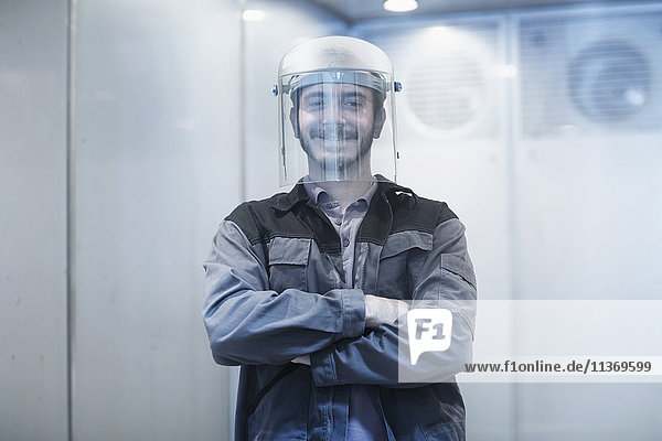 Porträt eines jungen männlichen Ingenieurs  der einen Helm in einem technischen Raum trägt und lächelt