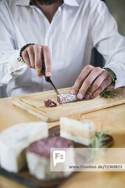 Mid section of a man cutting salami in the kitchen
