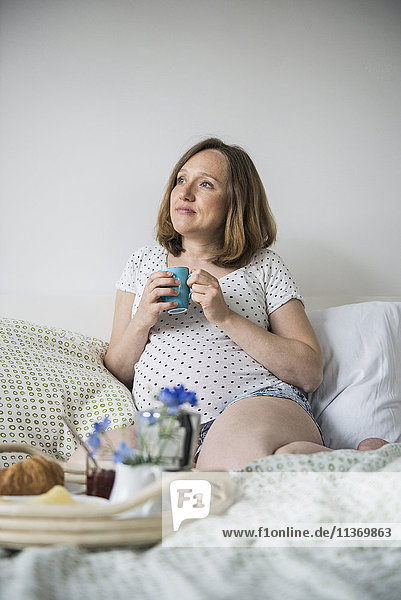 Schwangere Frau beim Frühstück im Bett