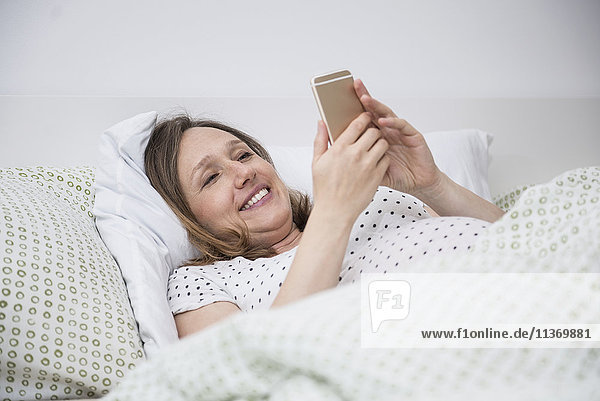 Pregnant woman lying in bed and using on mobile phone