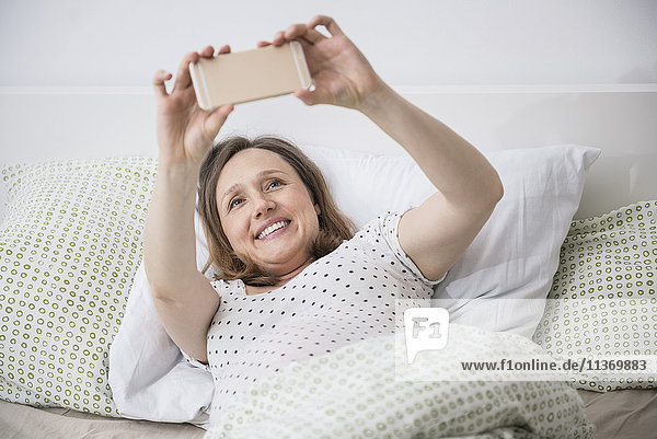 Pregnant woman lying in bed and taking selfie on mobile phone
