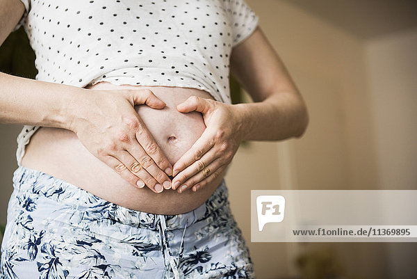 Mittelteil einer schwangeren Frau  die mit den Händen auf dem Bauch eine Herzform bildet