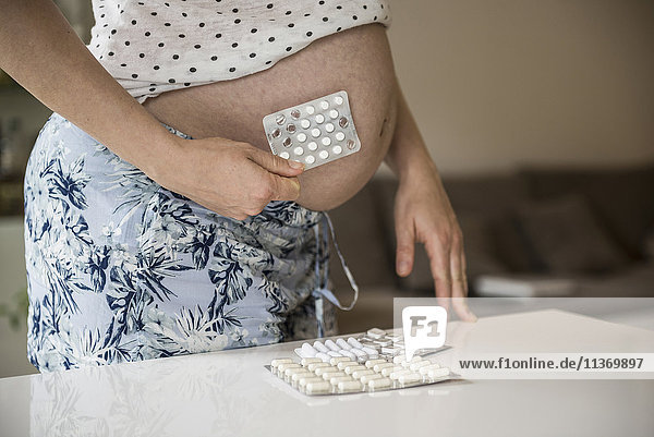 Mittelteil einer schwangeren Frau  die eine Blisterpackung vor ihrem Bauch hält