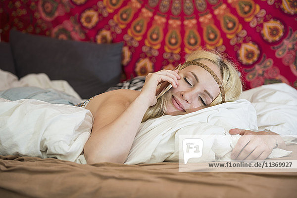 Schöne junge Frau  die im Schlafzimmer mit ihrem Smartphone telefoniert