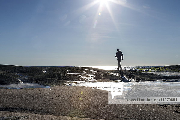 Silhouette einer Person  die an einer felsigen Küste spazieren geht