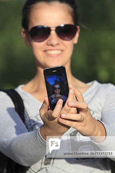 Junge Frau  die einen Selfie mit ihrem Smartphone nimmt.