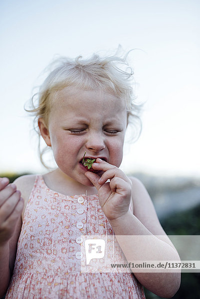 Mädchen macht Gesicht beim Essen einer Erdbeere