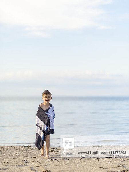 Junge in Handtuch eingewickelt am Strand