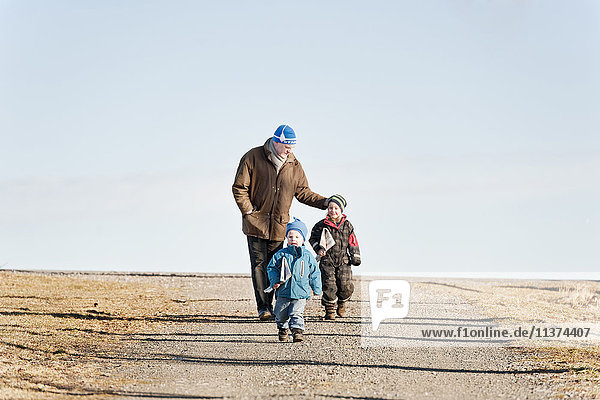 Grandfather and grandchildren walking along rural road