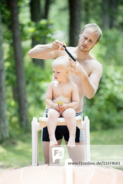 Father cutting hair of son in garden