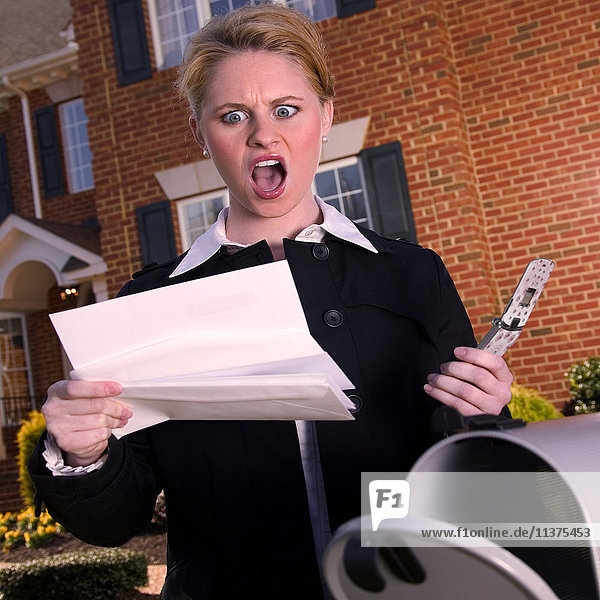 Wütende Frau liest Post am Briefkasten