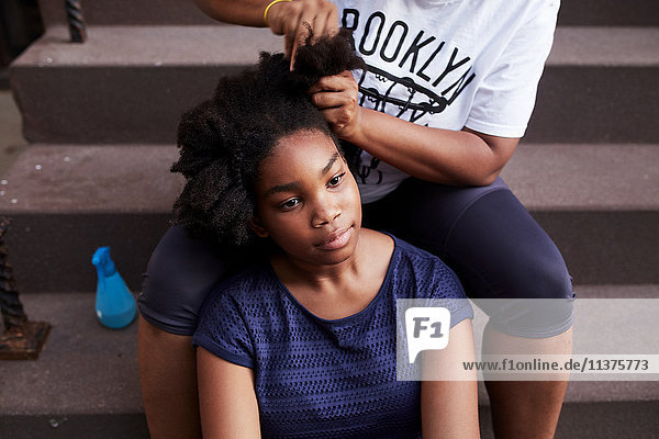 Schwarze Mutter frisiert die Haare ihrer Tochter auf der Treppe