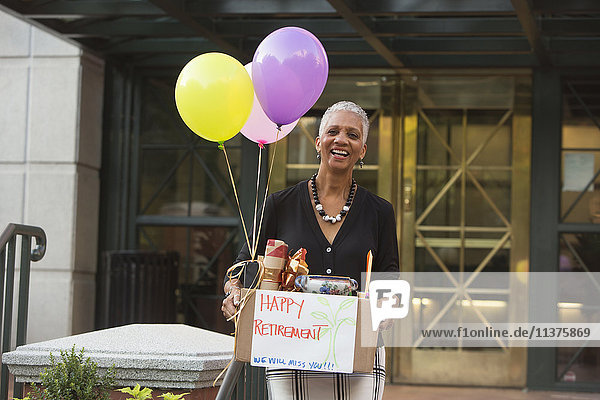 Black woman carrying belongings with happy retirement sign and balloons
