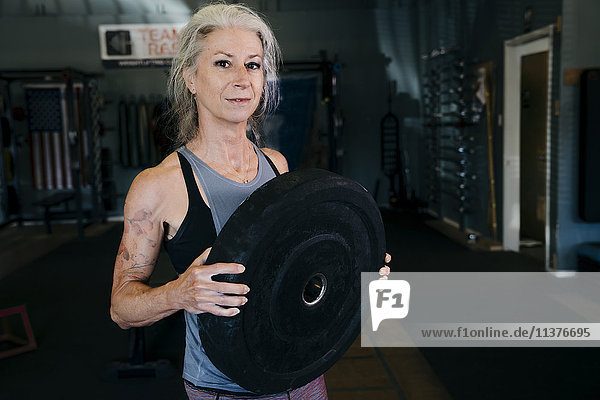 Caucasian woman holding large weight in gymnasium