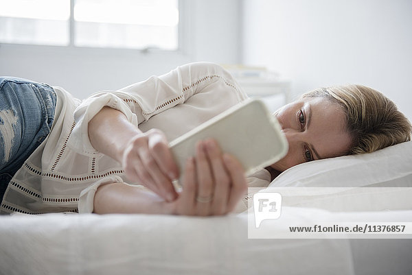 Caucasian woman laying on bed texting on cell phone