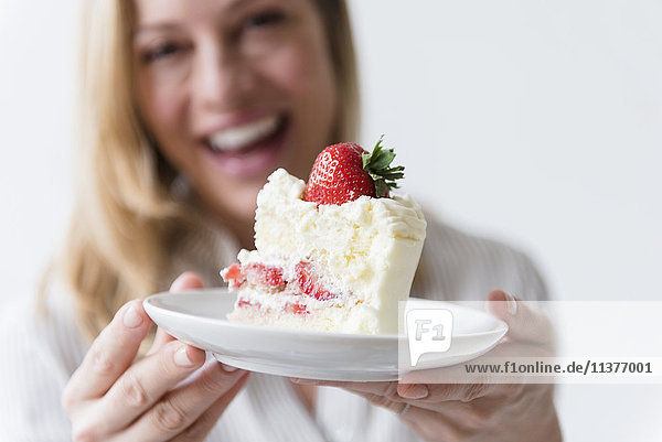 Kaukasische Frau hält ein Stück Vanillekuchen mit Erdbeere