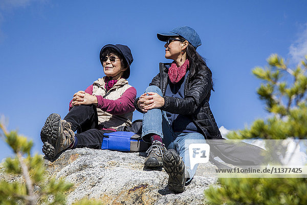 Older Japanese mother and daughter sitting on rock