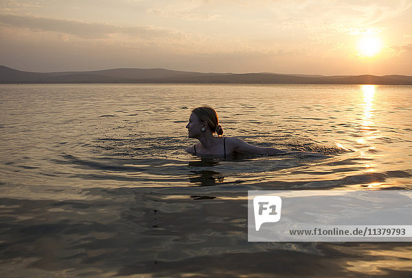 Kaukasische Frau schwimmt im See bei Sonnenuntergang