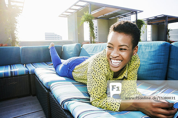 Black woman laying on rooftop sofa laughing