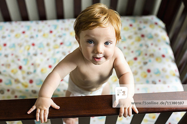 Porträt eines neugierigen kaukasischen kleinen Jungen in einem Kinderbett